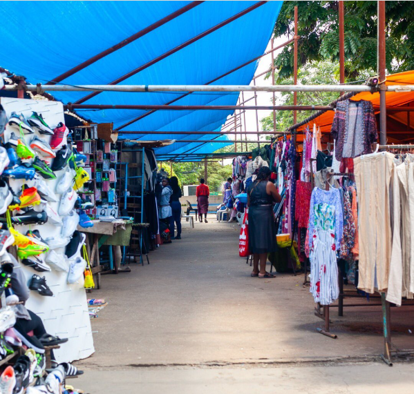 Flea market walkway with vendor tables and clothing stalls
